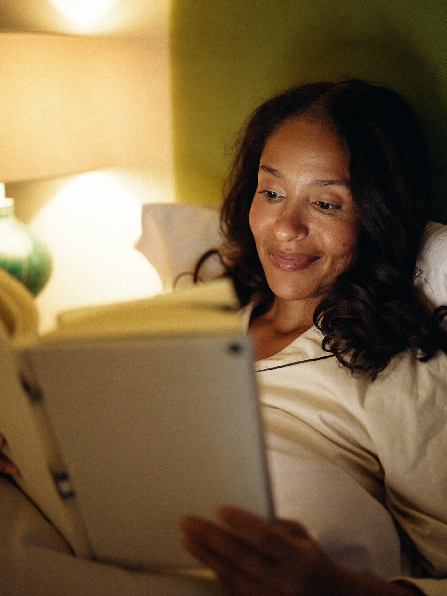 A woman reading calmly in bed by lamplight